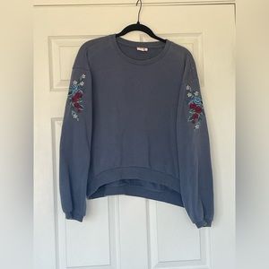 Blue sweater with embroidered flowers on the sleeves.
